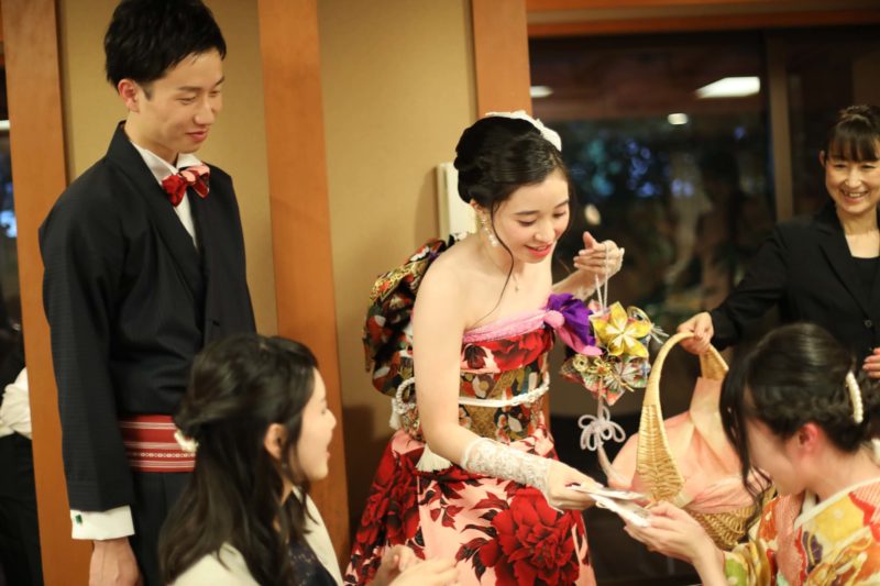新郎は着物スーツ、新婦は振袖ドレスといった装いでお色直しからの入場。
中座の中に、上映したプロフィールムービーは自ら出演してゲストにお色直しの衣装当てクイズを出すなど、こだわりの演出&主演&監督!
クイズに当たったゲストには景品を配りながら、各テーブルをまわり、ひとりひとりと言葉を交わし、記念撮影をしました。