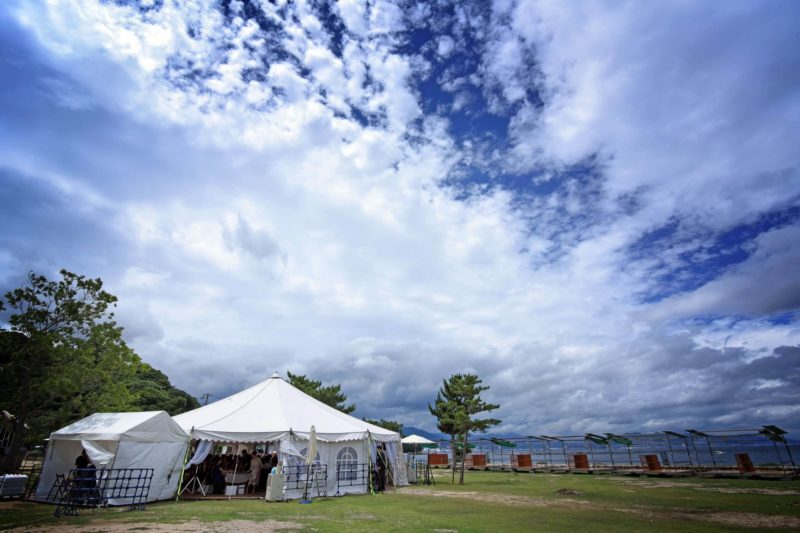 神社からマイクロバスで、島内にある包ヶ浦自然公園に移動。そこには、ふたりの披露宴のためのテントが出現!
たいへん珍しいスタイルのパーティにゲストの期待も最高潮に。